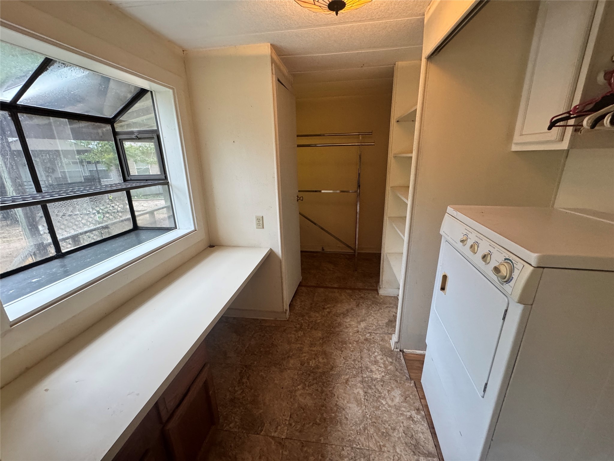 106 Westlake Road Trinity, TX 75862 - Photo 18 of 36 This photo shows a utility room with a washer, shelving, and a folding counter under a large window. The space is bright, with tiled flooring and ample storage, ideal for laundry and organization.