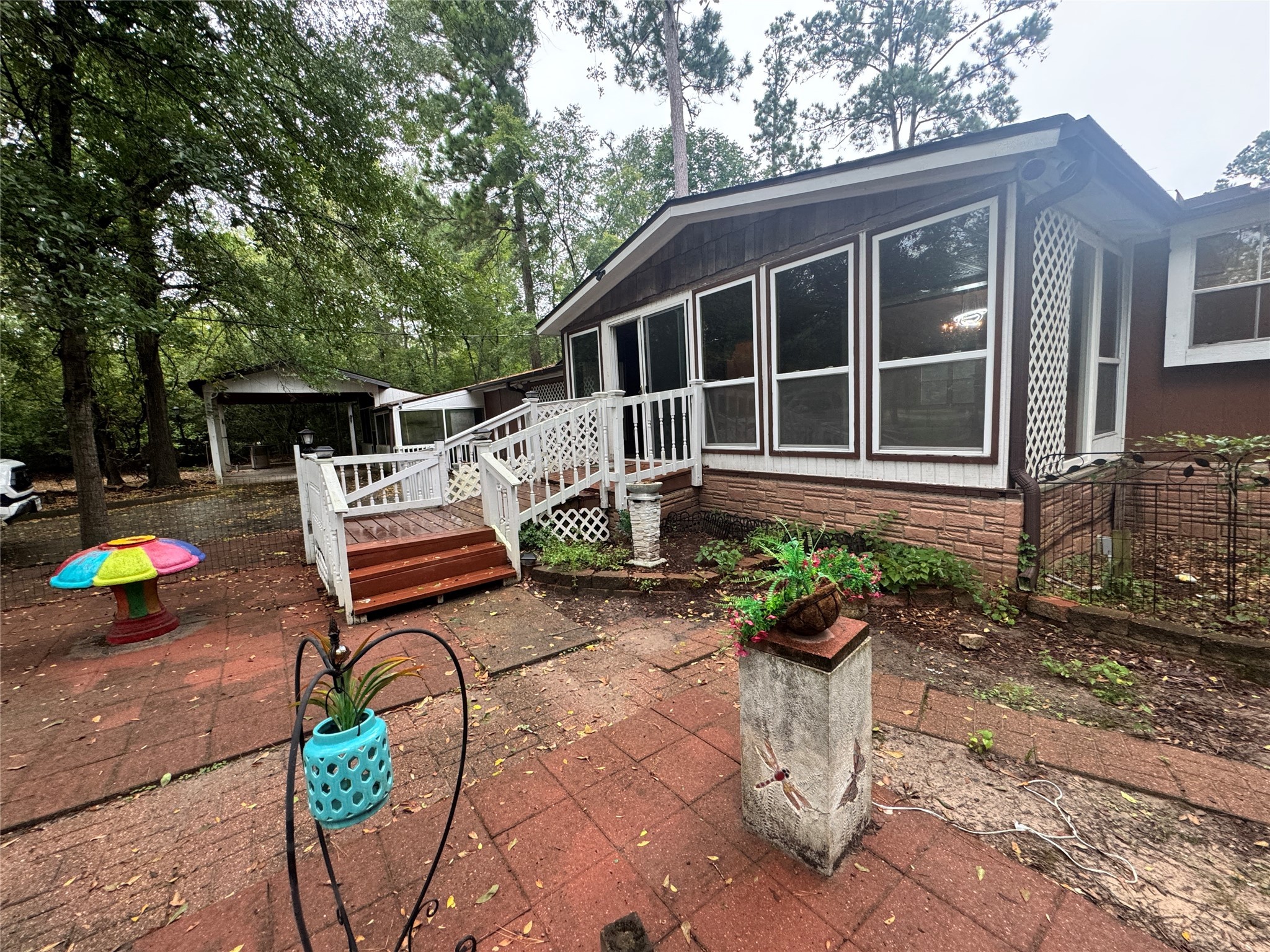 106 Westlake Road Trinity, TX 75862 - Photo 2 of 36 Charming home with a cozy enclosed patio featuring large windows, surrounded by lush greenery. The outdoor space is paved and includes a small garden area, perfect for relaxation or entertaining.