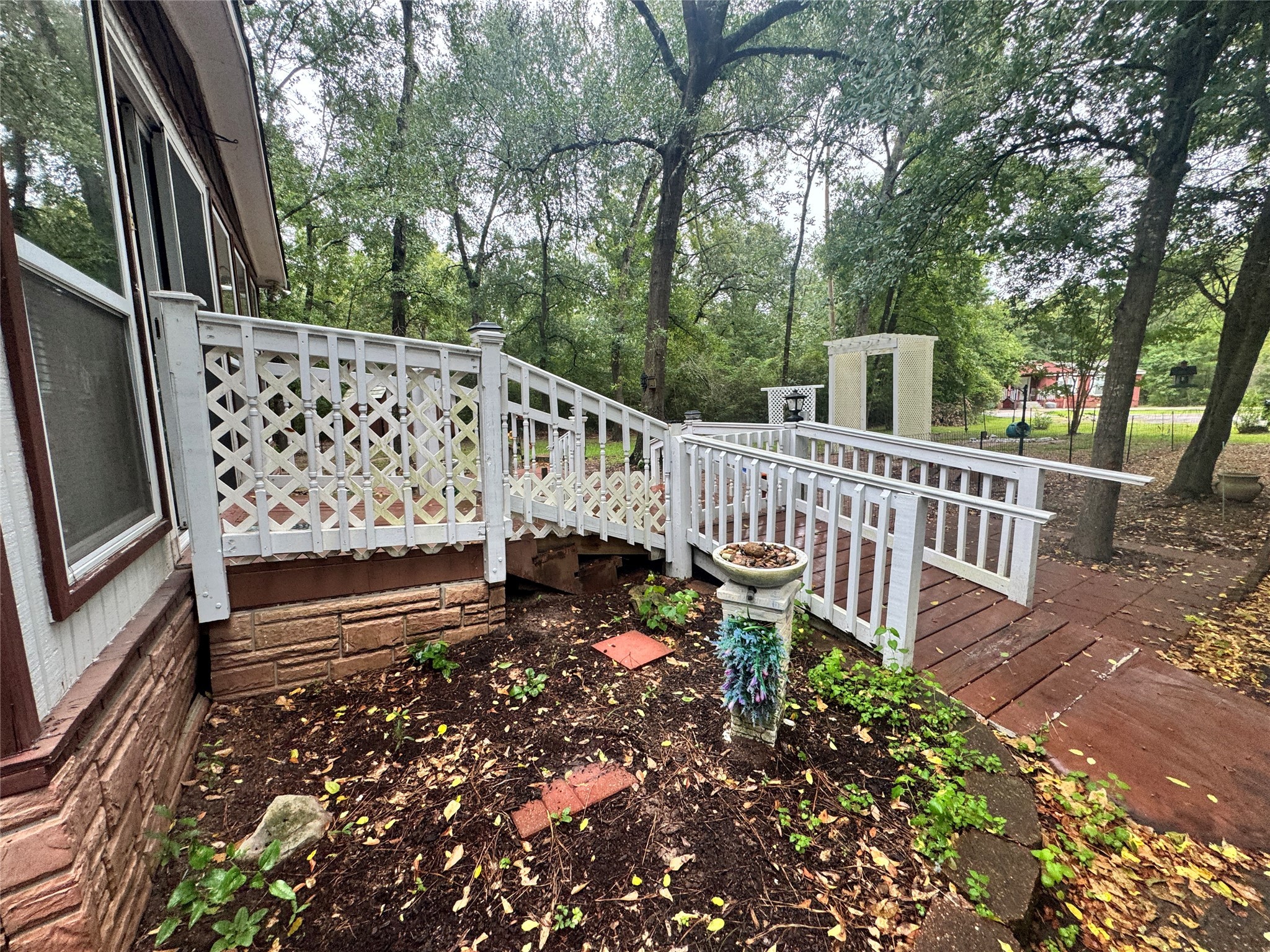 106 Westlake Road Trinity, TX 75862 - Photo 5 of 36 Charming outdoor space with a wooden deck and white lattice railing, surrounded by lush greenery. Ideal for relaxing or entertaining, with a rustic touch and a peaceful woodland backdrop.