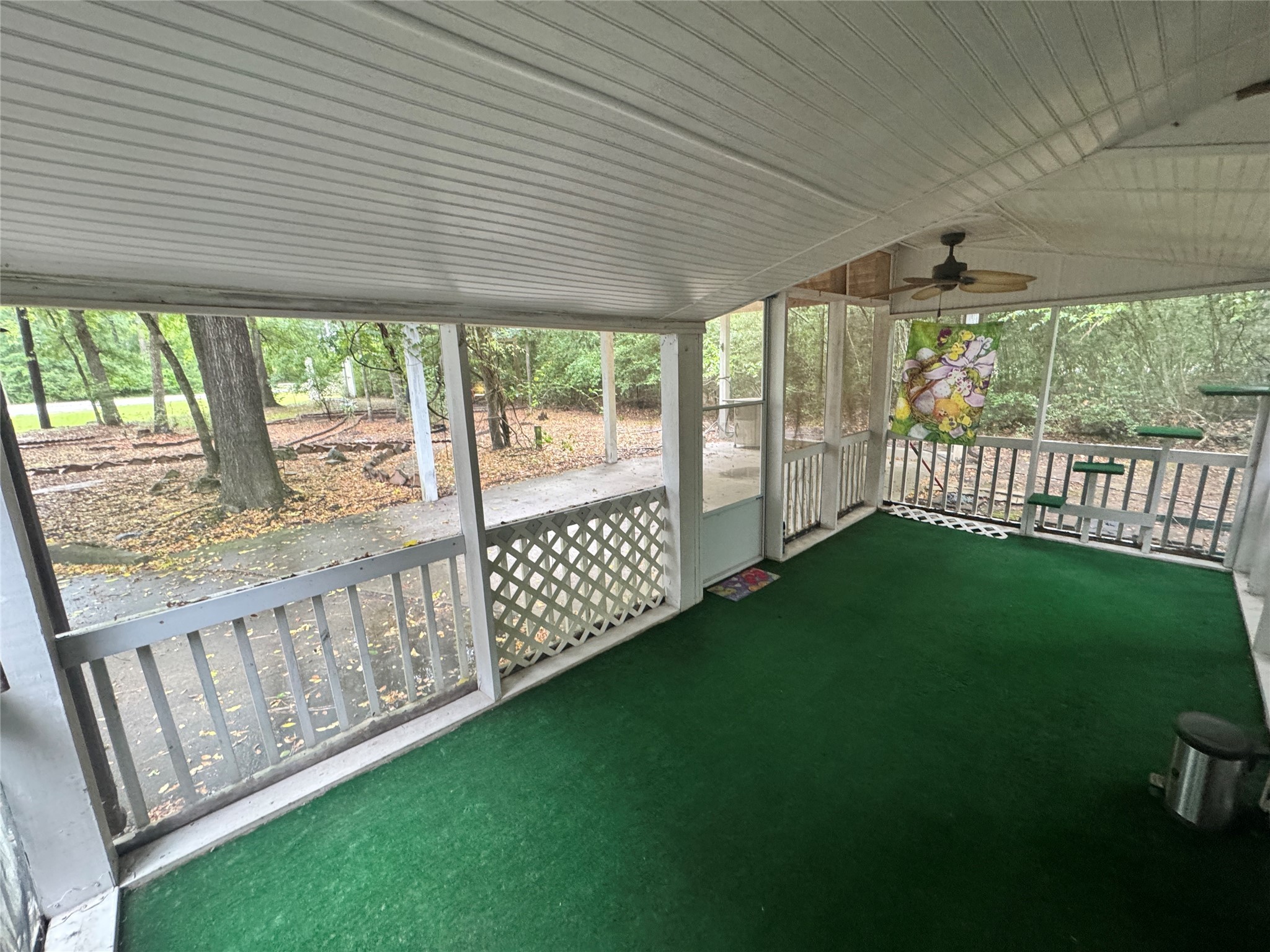 106 Westlake Road Trinity, TX 75862 - Photo 9 of 36 This photo shows a screened-in porch with green carpeting, a white ceiling, and a ceiling fan. It overlooks a wooded area, offering a peaceful, outdoor living space.