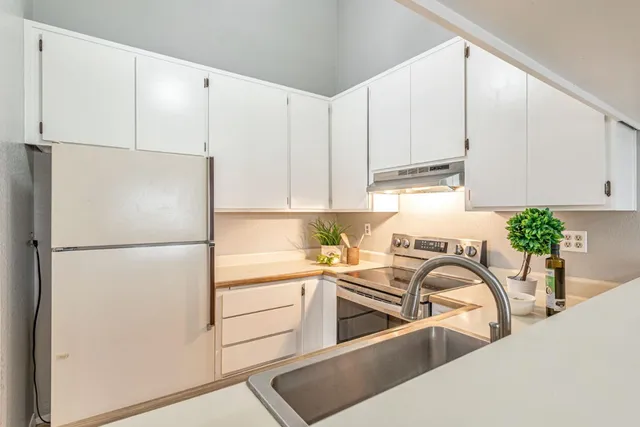 a kitchen with stainless steel appliances a refrigerator a sink a stove and white cabinets
