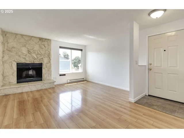 a view of an empty room with wooden floor fireplace and a window