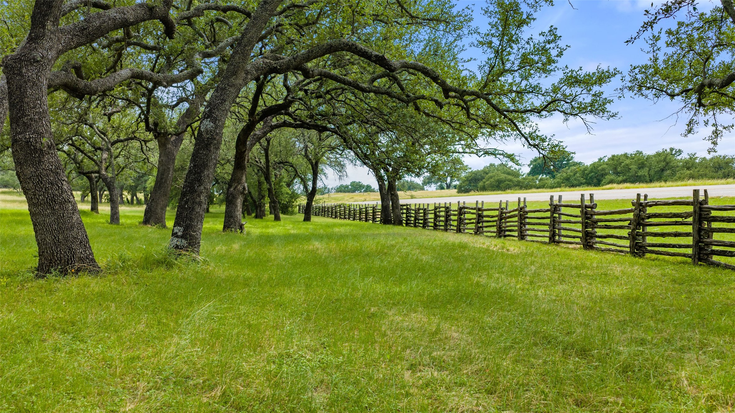 8400 Ranch Road 1431 Marble Falls, TX 78654 - Photo 26 of 30 A picturesque, green expanse bordered by mature trees and a rustic split-rail fence, offering serene natural beauty.
