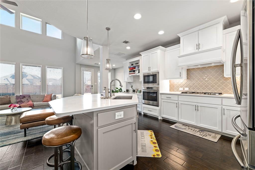 16541 Sweetgum Road Frisco, TX 75033 - Photo 7 of 26 Kitchen featuring a large island with sink, white shaker cabinetry, stainless steel appliances, a textured tile backsplash, and dark wood-finish flooring
