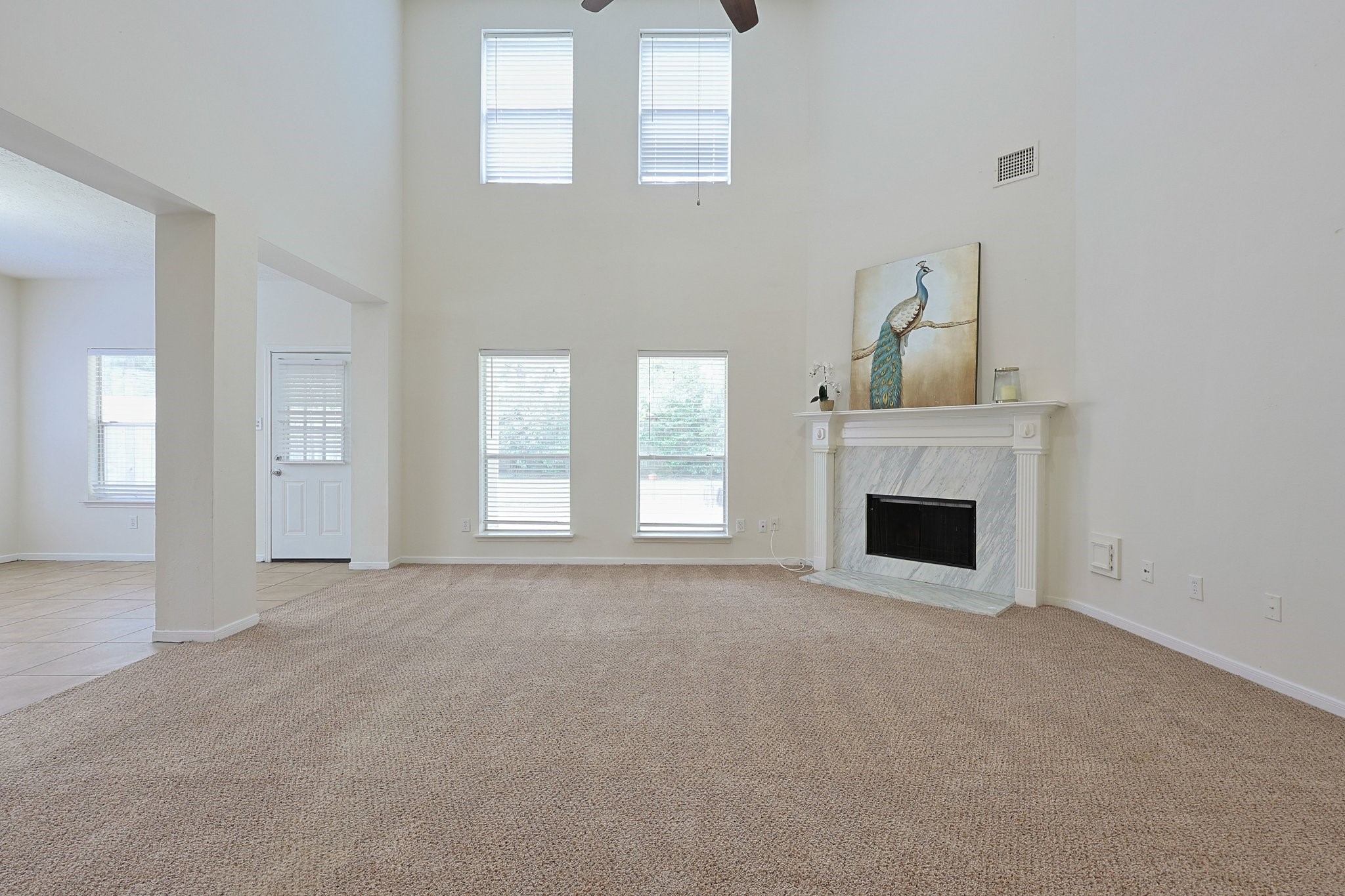 23019 Eastgate Village Drive Spring, TX 77373 - Photo 7 of 46 This spacious living room features high ceilings, large windows for natural light, a cozy fireplace with a decorative mantel, and neutral carpeting. Adjacent to the living area, there's easy access to a tiled entryway. Perfect for relaxation and entertaining.