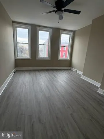 an empty room with wooden floor ceiling fan and windows