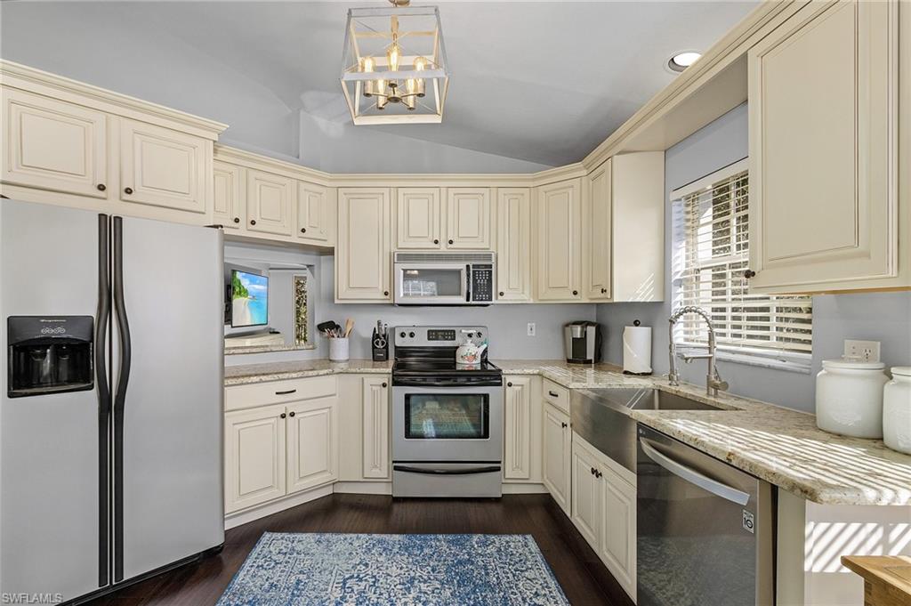 3785 Fieldstone Boulevard, Unit 208 Naples, FL 34109 - Photo 5 of 26 Kitchen featuring cream cabinets, a farmers sink, vaulted ceiling, appliances with stainless steel finishes, and wood floors