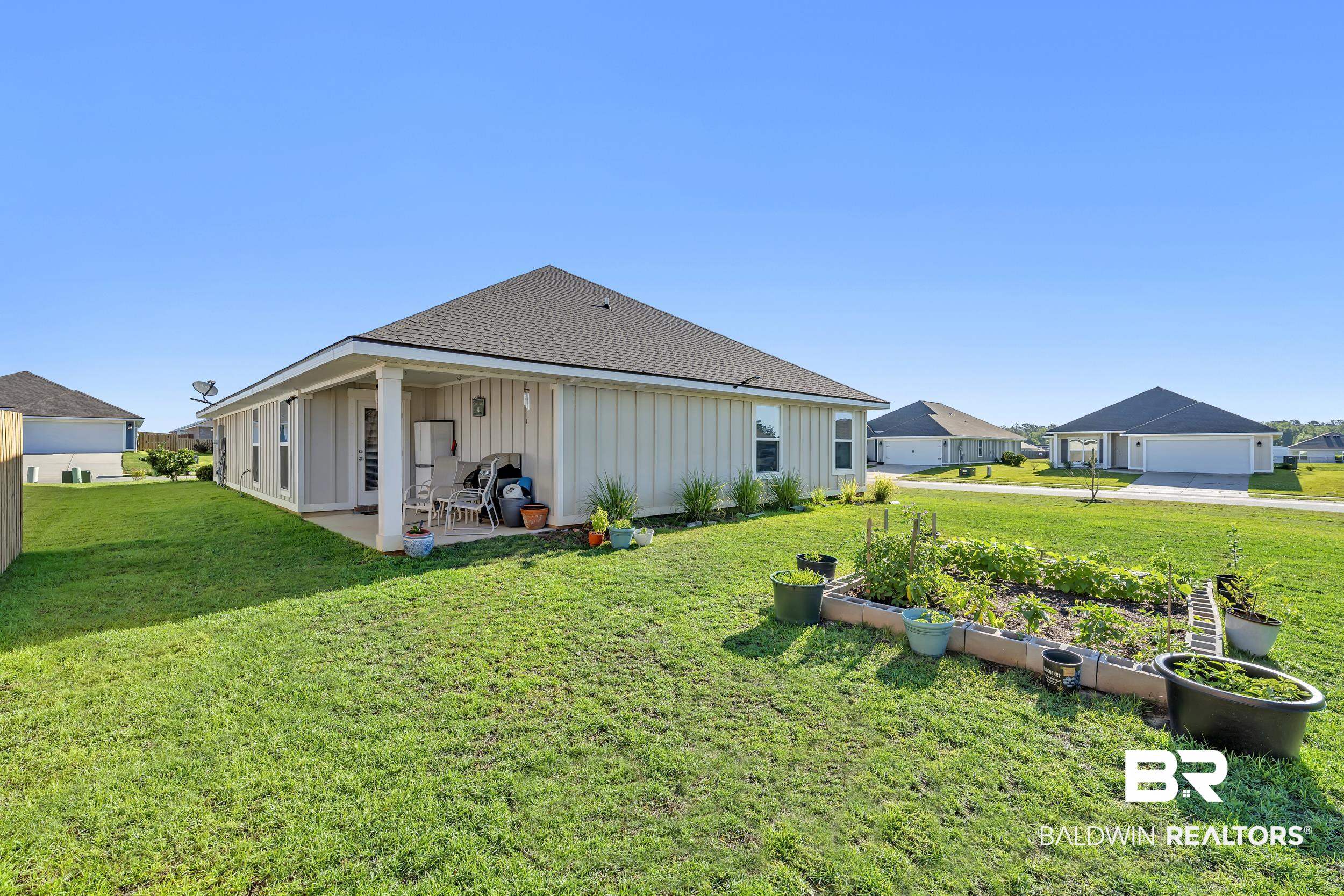 1228 Caper Avenue Foley, AL 36535 - Photo 35 of 54 Expansive rear yard featuring a covered patio, a raised garden bed, and a well-maintained lawn