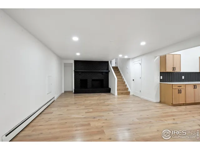 a view of an empty room with wooden floor and kitchen