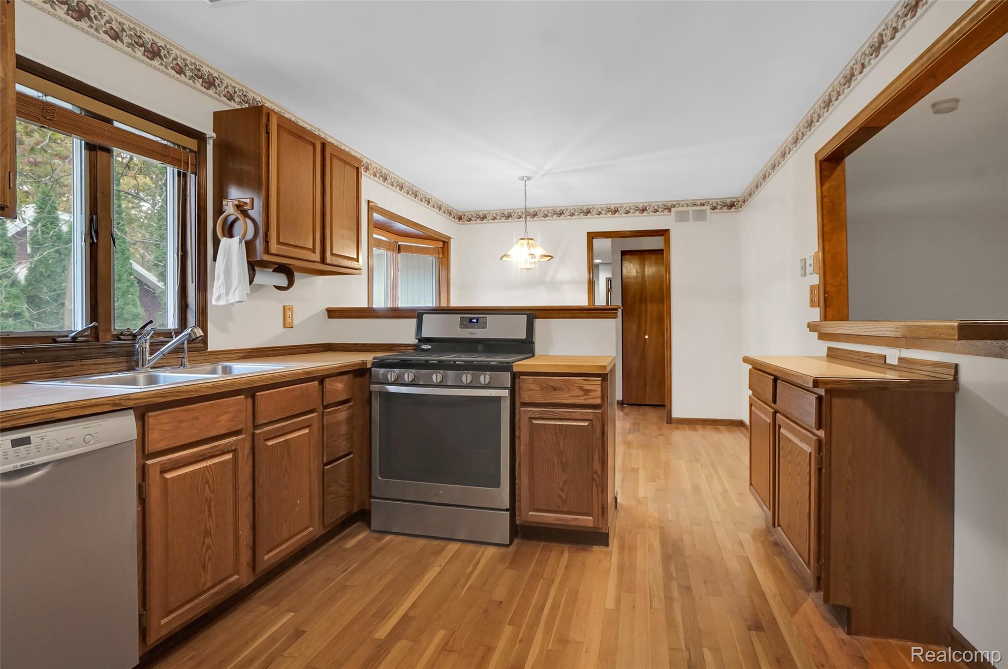 1431 East Commerce Road Commerce Township, MI 48382 - Photo 9 of 27 Kitchen featuring stainless steel gas stove, brown cabinetry, dishwashing machine, a peninsula, and decorative light fixtures