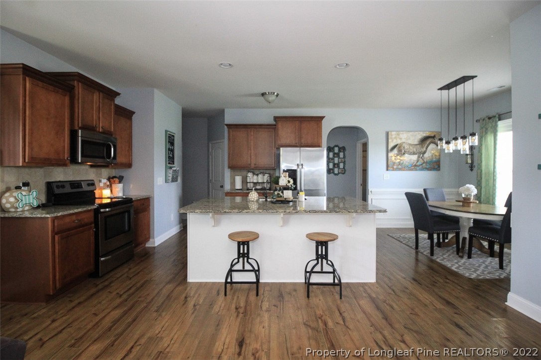 3549 Thrower Road Hope Mills, NC 28348 - Photo 7 of 38 a kitchen with stainless steel appliances granite countertop a stove a refrigerator a kitchen island a dining table and chairs with wooden floor