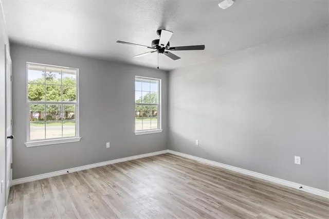 an empty room with wooden floor ceiling fan and windows