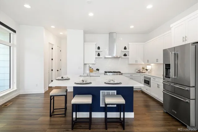 a kitchen with stainless steel appliances granite countertop a sink a stove a refrigerator and white cabinets with wooden floor