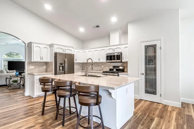 a kitchen with stainless steel appliances a stove top oven a refrigerator a sink and white cabinets with wooden floor