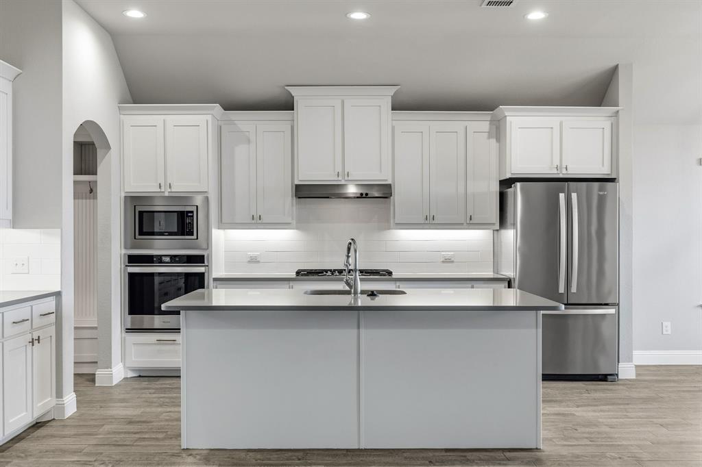 915 Timber Ridge Drive Justin, TX 76247 - Photo 9 of 39 Modern kitchen featuring white shaker-style cabinetry, stainless steel appliances, a center island with a sink, and recessed lighting