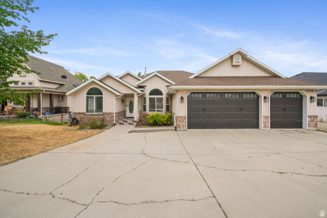 Stucco exterior with stone accents, a multi-car garage, arched window features, a covered entry, and a paved driveway