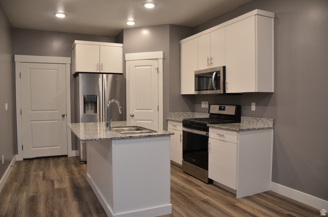 1842 South 1280th Street West Logan, UT 84321 - Photo 5 of 21 Kitchen featuring white shaker cabinetry, stainless steel appliances, speckled granite countertops, a central island with an undermount sink, and wood-finish flooring