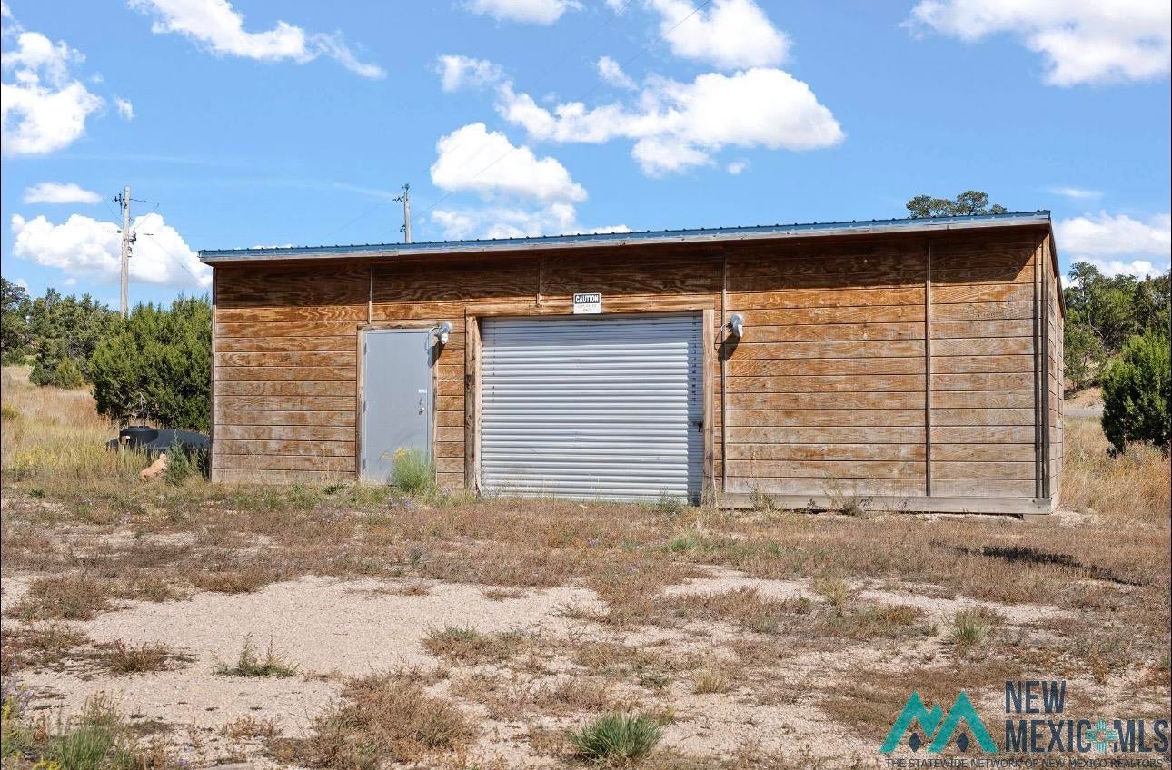371 Candy Kitchen Road Candy Kitchen, NM 87357 - Photo 28 of 49 Freestanding utility building featuring wood panel siding, a metal roll-up door, a separate pedestrian entry, and a metal roof