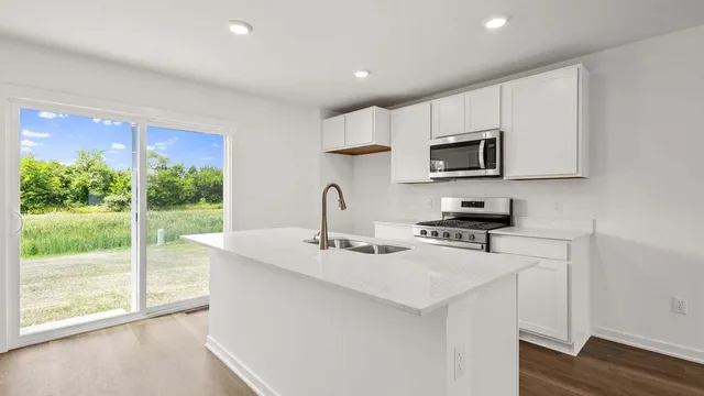 a kitchen with stainless steel appliances granite countertop a stove a sink a microwave a refrigerator and white cabinets with wooden floor