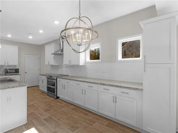 a large kitchen with stainless steel appliances granite countertop a stove a sink dishwasher and white cabinets with wooden floor