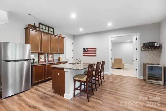 a kitchen with stainless steel appliances granite countertop a refrigerator a sink a stove a dining table and chairs with wooden floor