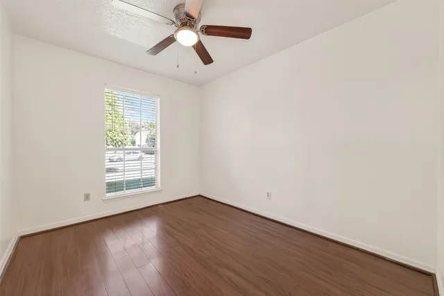 an empty room with wooden floor fan and windows