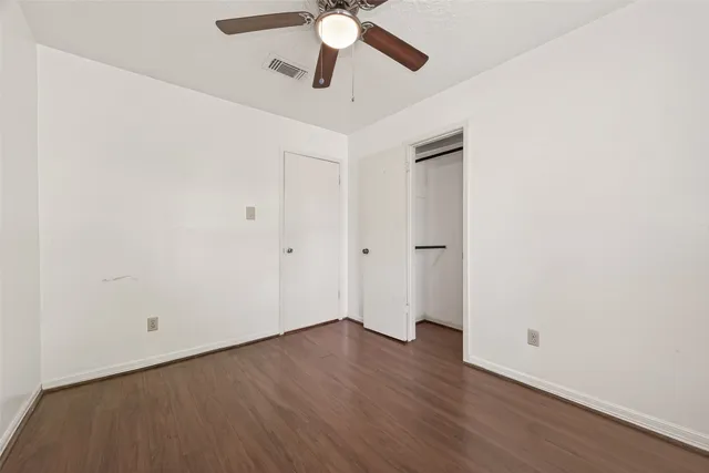 an empty room with wooden floor ceiling fan and window