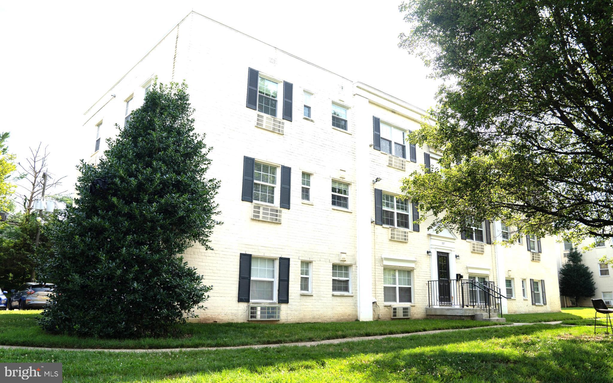 a view of a white house next to a yard with big trees