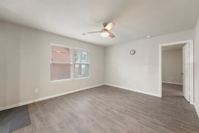 an empty room with wooden floor fan and windows