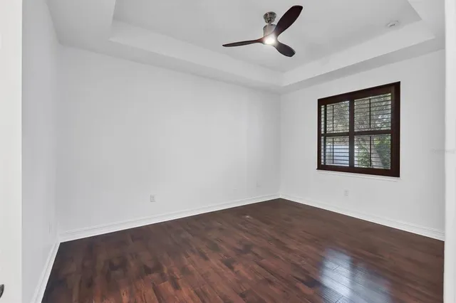 an empty room with wooden floor chandelier fan and windows