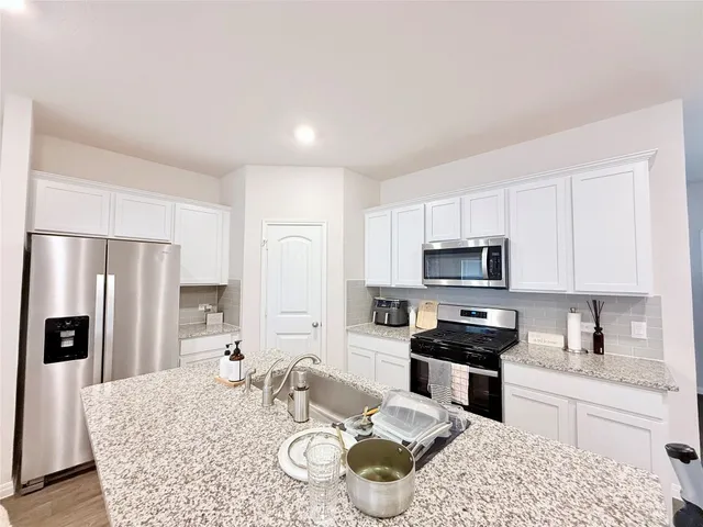 a kitchen with stainless steel appliances granite countertop a stove a sink a refrigerator a dining table and chairs