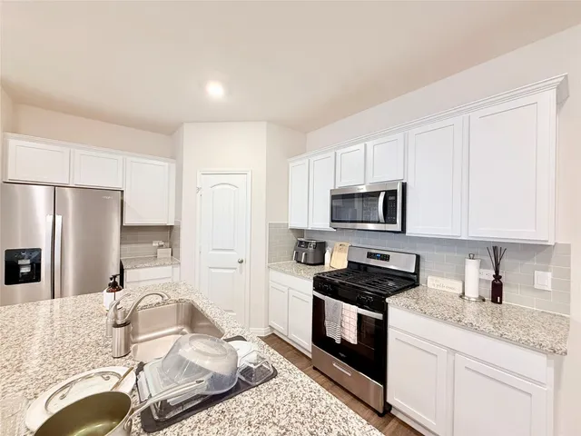 a kitchen with granite countertop kitchen island stainless steel appliances a stove refrigerator sink and cabinets