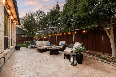 a view of a patio with couches and chairs under an umbrella with large trees