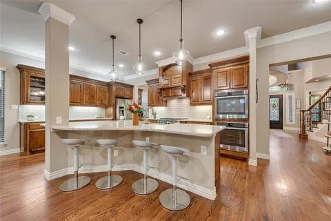 a large kitchen with stainless steel appliances kitchen island granite countertop wooden floors and a view of living room