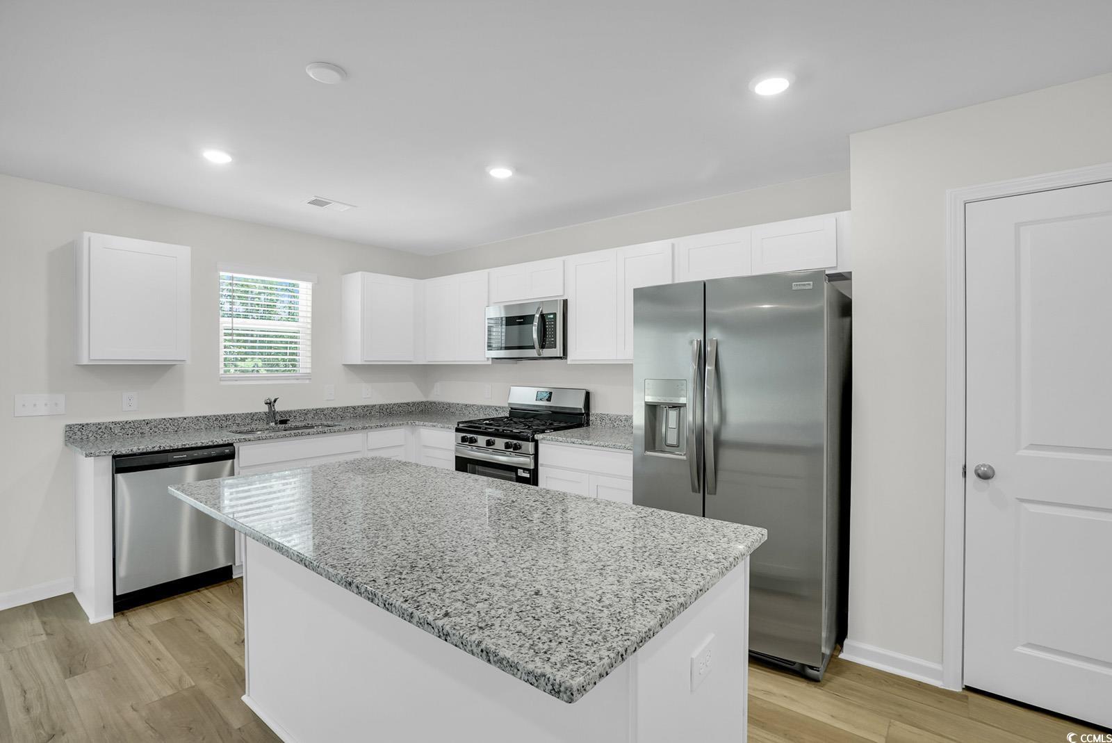 1113 Hainer Place Drive Conway, SC 29526 - Photo 2 of 28 Kitchen with appliances with stainless steel finishes, light stone counters, white cabinets, light wood-style floors, and a center island