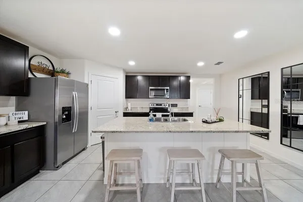 a kitchen with stainless steel appliances granite countertop a sink a stove a refrigerator cabinets and chairs