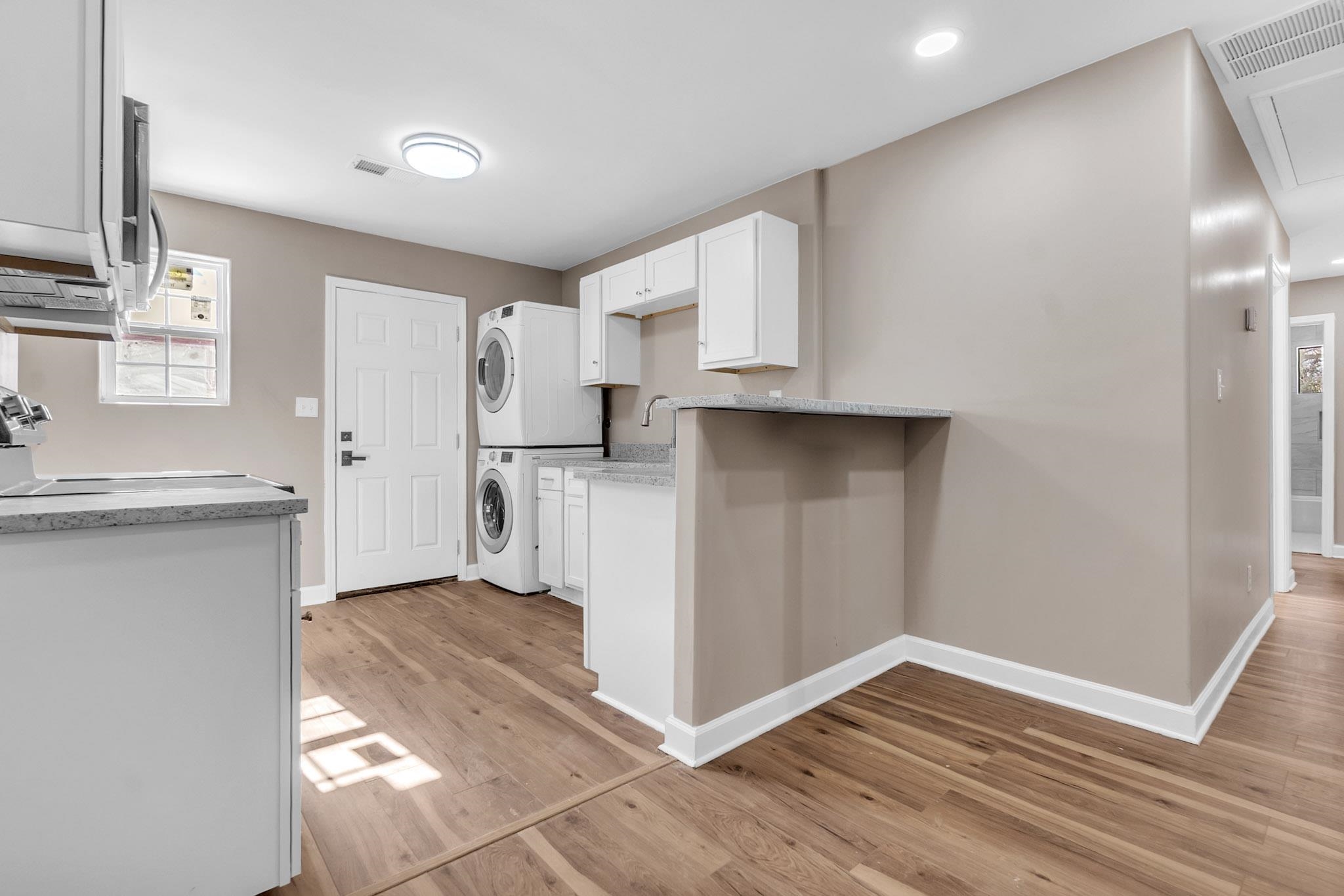 375 Pope Street Memphis, TN 38112 - Photo 16 of 19 Kitchen with white cabinets, light wood-style flooring, stove, stacked washing machine and dryer, and stainless steel microwave