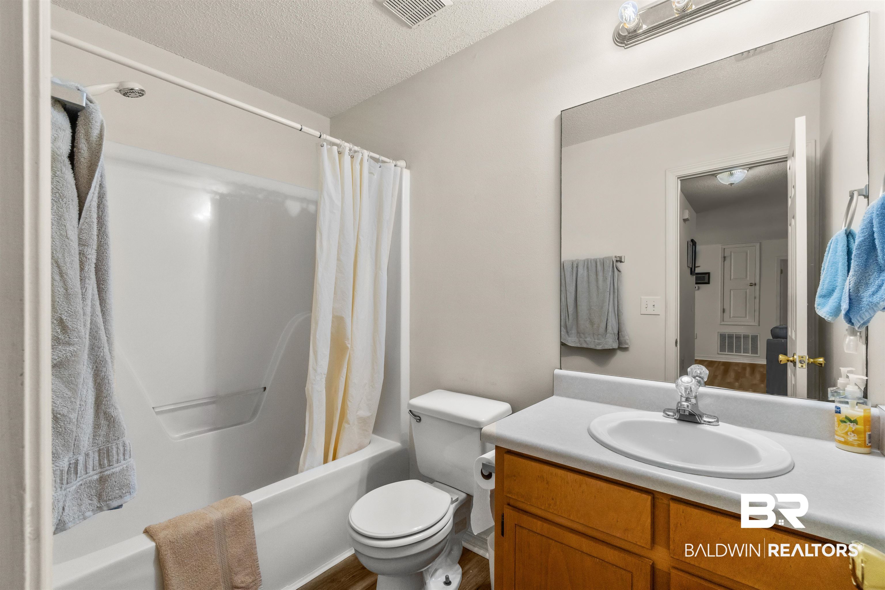 35893 Pine Road South Stapleton, AL 36578 - Photo 23 of 31 Full bathroom featuring a white tub/shower combination, a toilet, a vanity with a white countertop and integrated sink, a wood-finish cabinet, and an expansive wall-mounted mirror