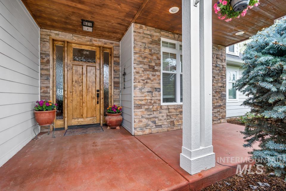 8271 Washoe Road Fruitland, ID 83619 - Photo 4 of 29 Inviting entryway featuring a wood-finish front door with decorative glass sidelights, stacked stone accents, white siding, a wood-finish ceiling, and a prominent white architectural column