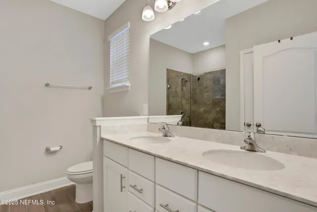 a bathroom with a granite countertop toilet a double vanity sink and a mirror