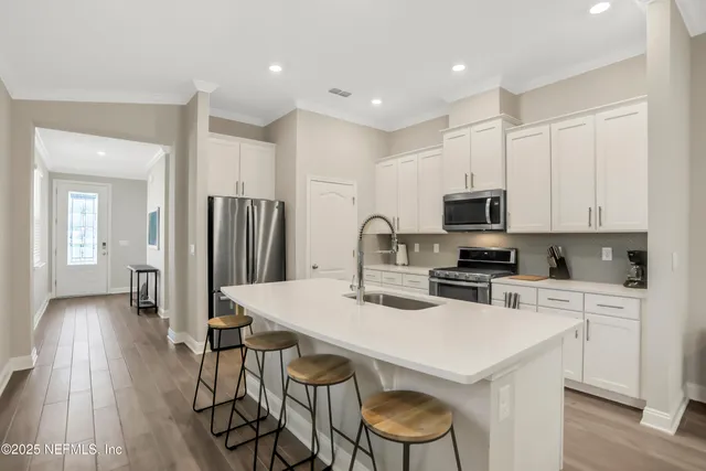 a kitchen with stainless steel appliances a stove a sink a refrigerator white cabinets and wooden floor