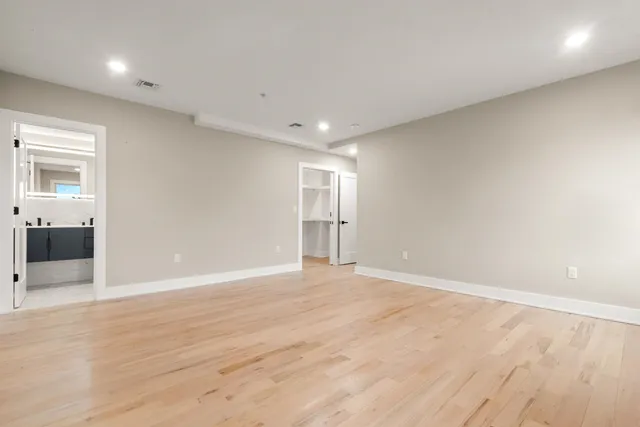 a view of an empty room with wooden floor and a bathroom