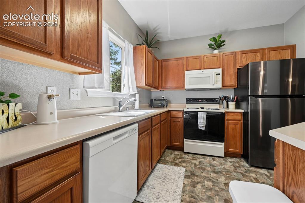 3715 Riviera Grove, Unit 101 Colorado Springs, CO 80922 - Photo 20 of 36 Kitchen featuring warm wood cabinetry, light-toned countertops, window with natural light, stainless steel refrigerator, and integrated white dishwasher