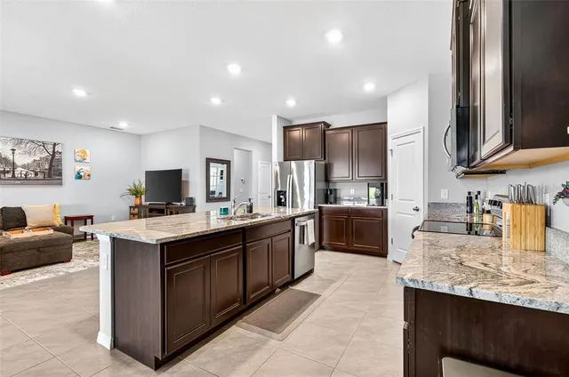 a large kitchen with stainless steel appliances granite countertop a stove top oven a sink dishwasher and a refrigerator with wooden cabinets