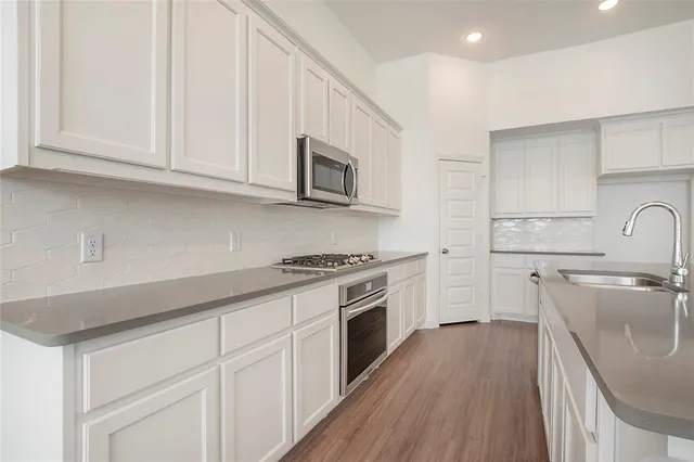 a kitchen with cabinets stainless steel appliances a sink and wooden floor