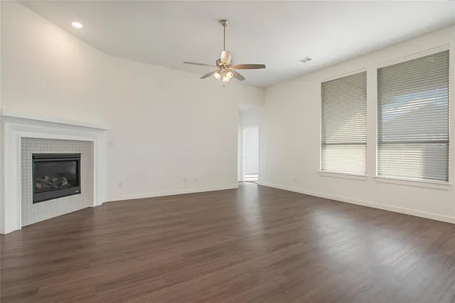 an empty room with wooden floor chandelier fan and windows