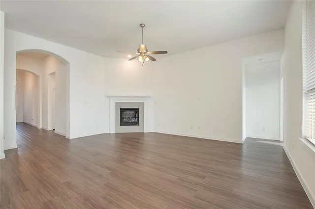 an empty room with wooden floor chandelier fan and windows