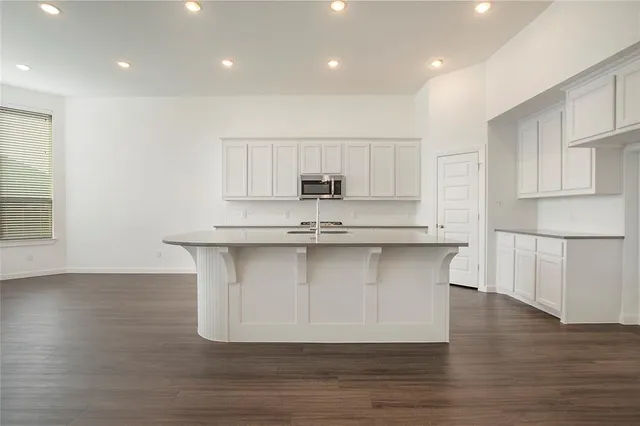 a large kitchen with granite countertop a stove top oven a sink and white cabinets with wooden floor