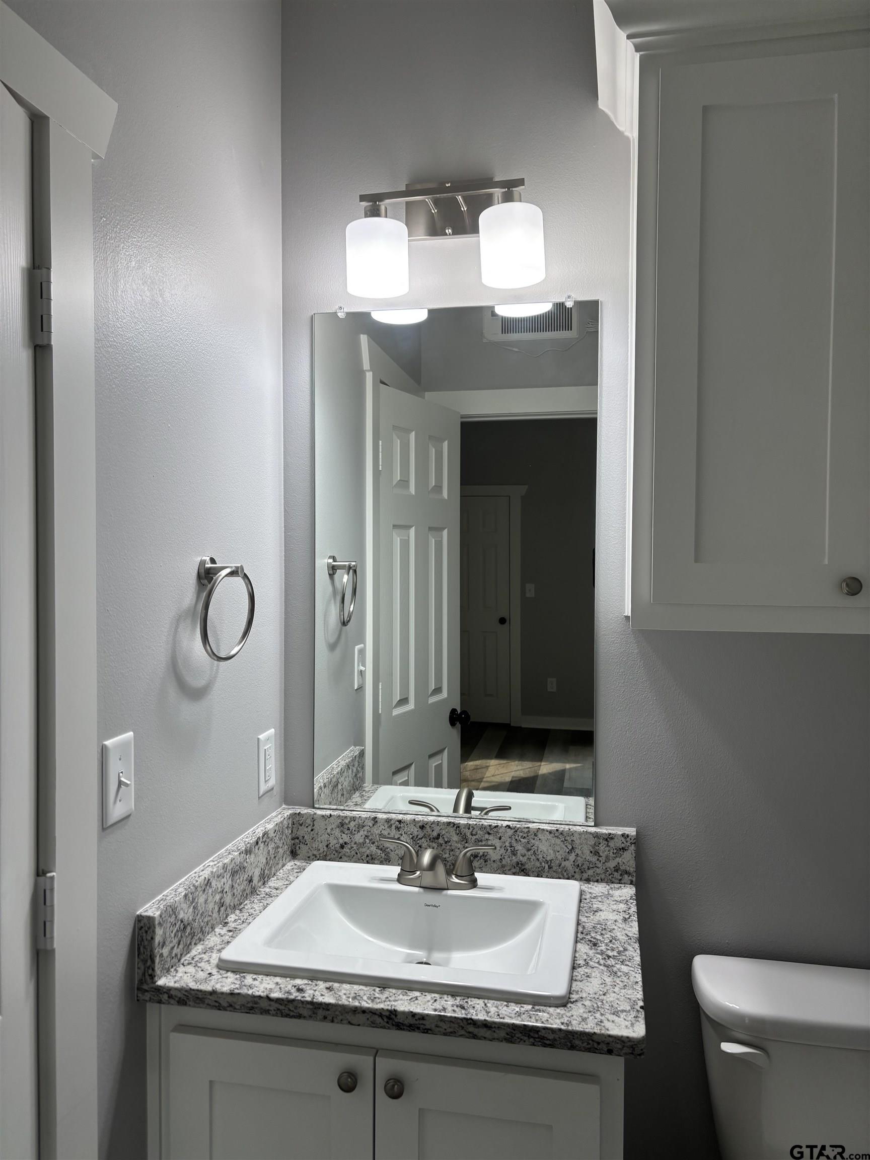 11571 19th Avenue, Unit 102 Tyler, TX 75708 - Photo 4 of 4 a bathroom with a granite countertop sink a toilet and a mirror