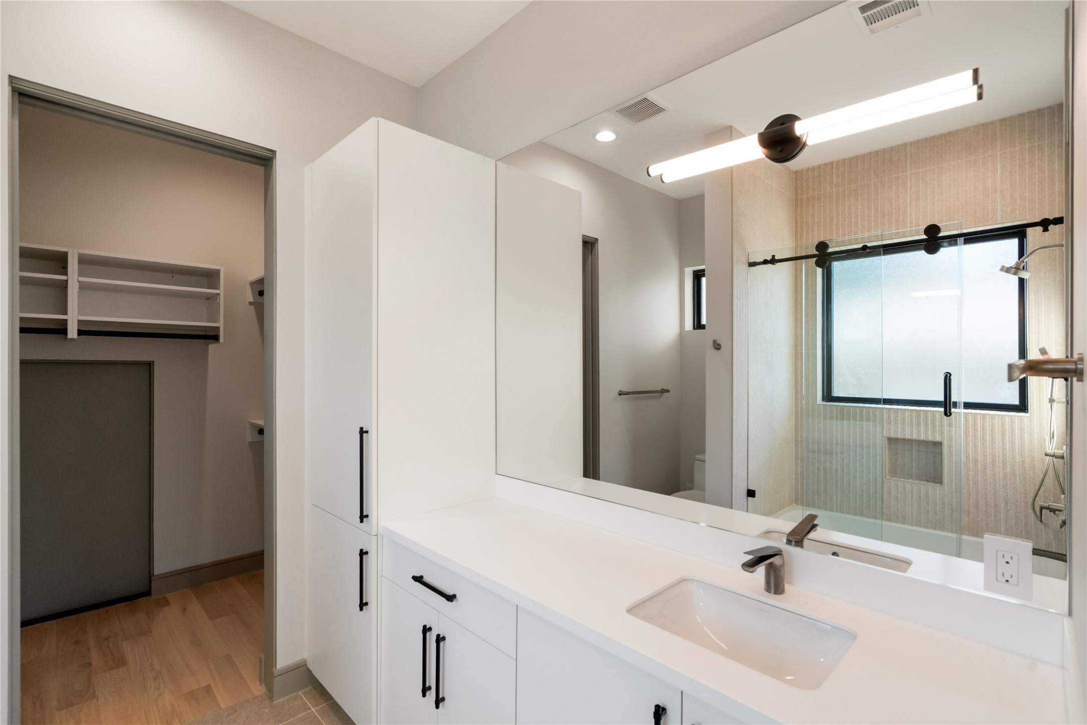 47 Pronghorn Place Spring, TX 77389 - Photo 26 of 44 This modern bathroom features a sleek design with a spacious vanity, large mirror, and ample storage. It includes a glass-enclosed shower and a separate closet area with built-in shelving, all in a neutral color palette for a clean and contemporary feel.